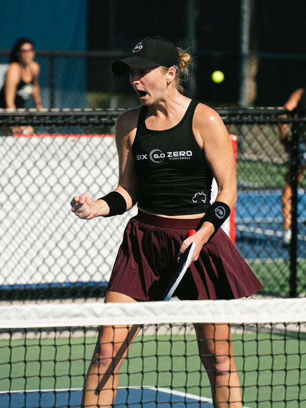 Tennis player on a court wearing a black tank top with 'Six Zero' branding.