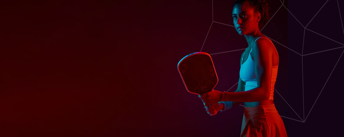 Woman holding a pickleball paddle against a dark background with geometric patterns
