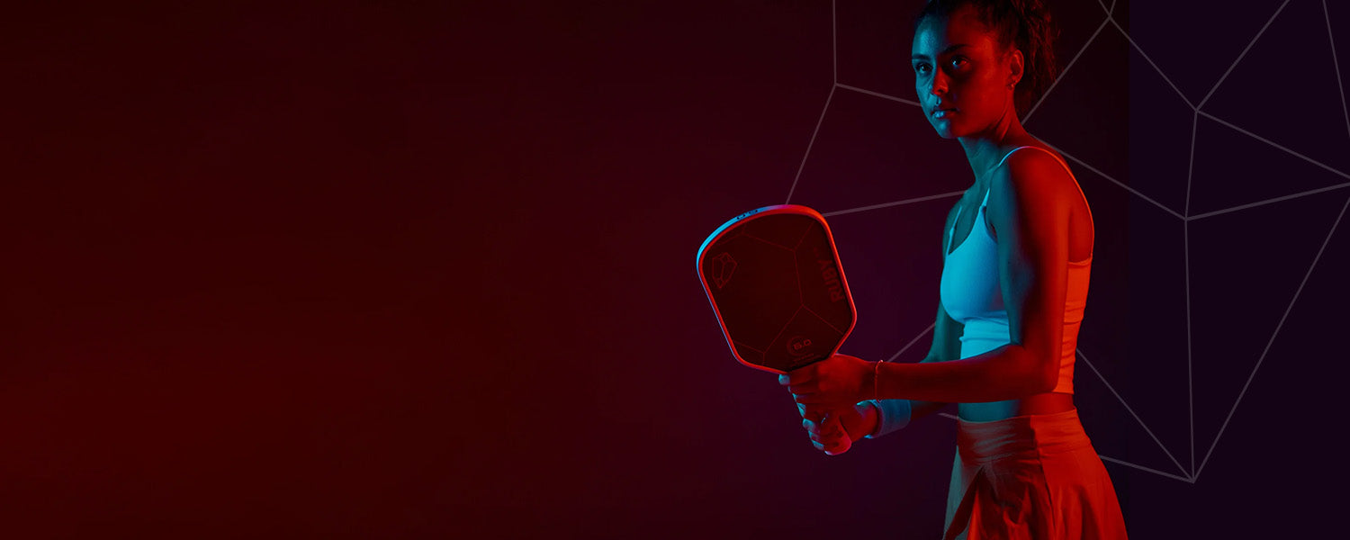 Woman holding a pickleball paddle against a dark background with geometric patterns